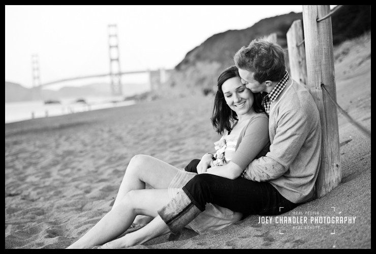 Soft Kisses at Baker Beach Young engaged couple sitting at Baker Beach with the Golden Gate Bridge