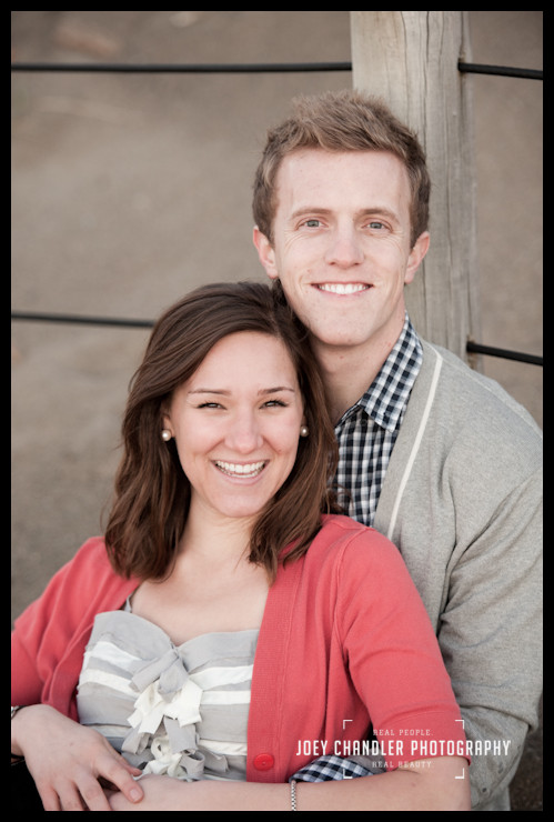 all smiles at Baker Beach Engaged Couple sitting against fence at Baker Beach in San Francisco