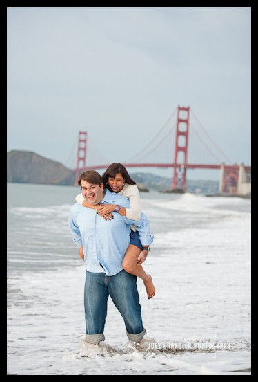 Team work at Baker Beach Man carring his fiance in the water at Baker Beach - San Francisco Engagement Photographer Joey Chandler