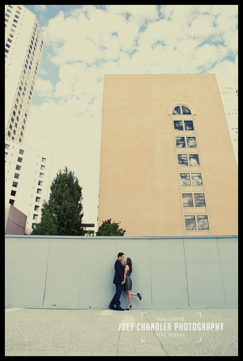 Happy kiss in San Francisco Witha tall building in the background leading up to blue sky and patchy clouds, a well-dressed couple looks at each other in a playful and loving way.