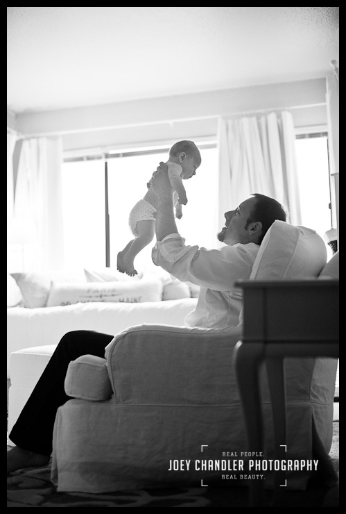 Dad holding his baby in his San Francisco home Black and white photo of dad holding his baby above his face admiringly.