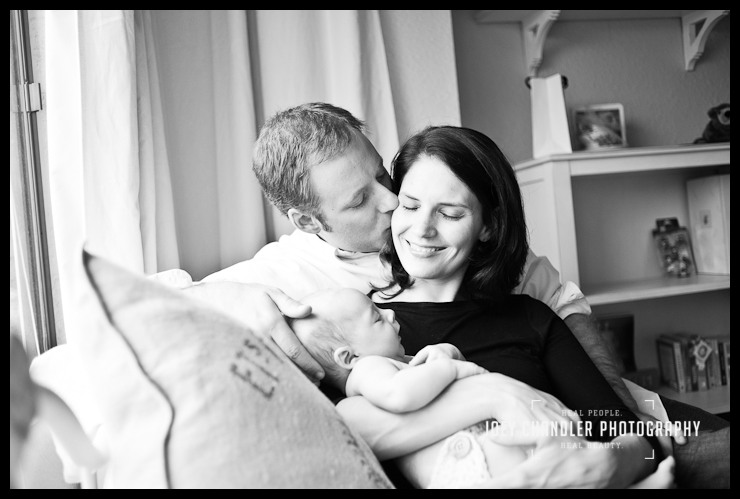 Love between mom, dad and newborn baby boy Portrait of family sitting on a couch with the father kissing his wife as she smiles, eyes closed, with their baby in her arms.